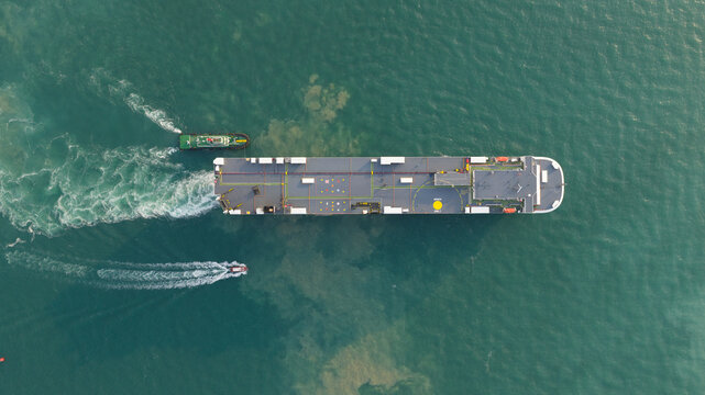 Aerial view of a large cargo ship and a tugboat navigating through turquoise waters with visible white wakes Laem Chabang, Chon Buri, Thailand.