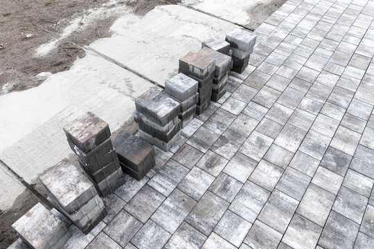 Stacks of gray concrete pavers arranged beside a partially completed paved walkway on a sand base showing texture, pattern and hardscape preparation for an outdoor patio or garden landscaping projects