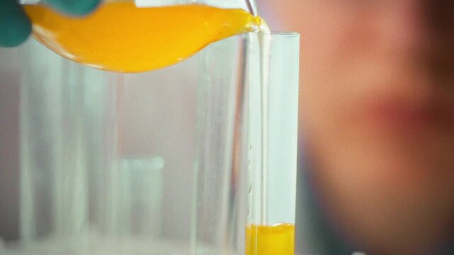 A scientist wearing protective gloves carefully pours a liquid into a test tube in a laboratory setting to conduct a precise experiment, showcasing meticulous research techniques daily