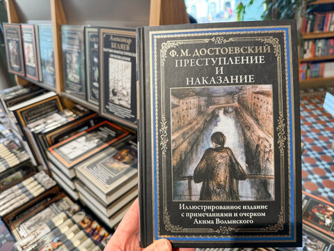 Saint Petersburg, Russia - April 27, 2026: Illustrated edition of Fyodor Dostoevsky's Crime and Punishment displayed in hand with bookshelves filled with various titles in background
