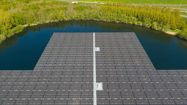 Aerial view of a large floating solar farm with rows of photovoltaic panels on a calm lake surrounded by lush green trees in Zwolle, Overijssel, Netherlands.