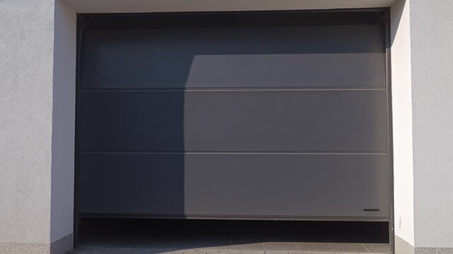 Sectional garage door is closing with storage items visible inside. Concept of residential garage access and property security