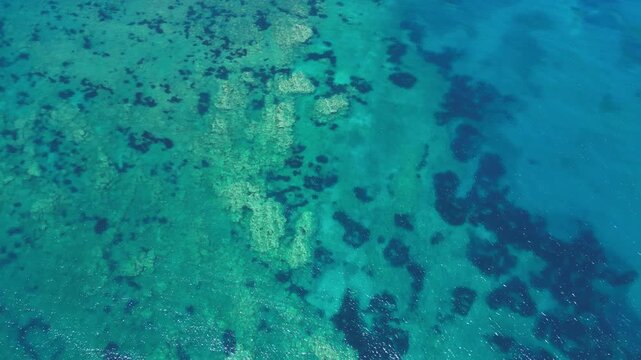 High angle view of turquoise ocean water with underwater rocks. Crystal clear sea surface with natural textures and sunlight reflections, perfect for summer travel or nature background.