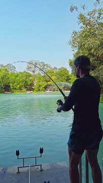 Vertical video. Man Reeling Strong Fish with Deeply Bent Rod Facing Open Lake First Person Feel Outdoor Angling Sport Excitement and Challenge