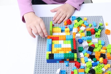 Naklejka premium Little girl playing with colorful building blocks at white table, closeup. Construction toy