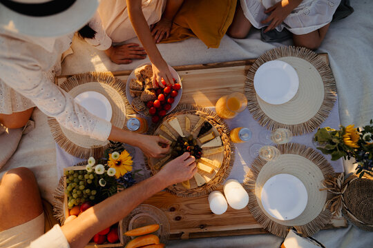 Top view of picknic blanket and hands picking food from plates.