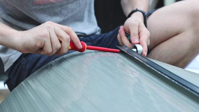 A craftsman installs side fasteners on a metal barn door using screwdrivers.