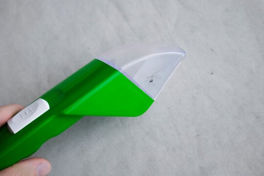Hand holding a green insect trap with a spider inside against textured fabric, demonstrating a friendly approach to insects.