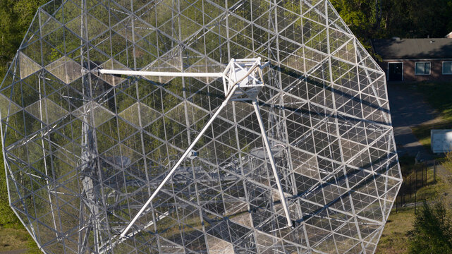 Aerial view of the Dwingeloo Radio Observatory showing the intricate metal lattice of the large parabolic dish surrounded by lush green forest in Dwingeloo, Drenthe, Netherlands.