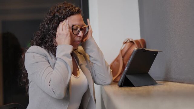 Stressed businesswoman suffering from headache working on tablet