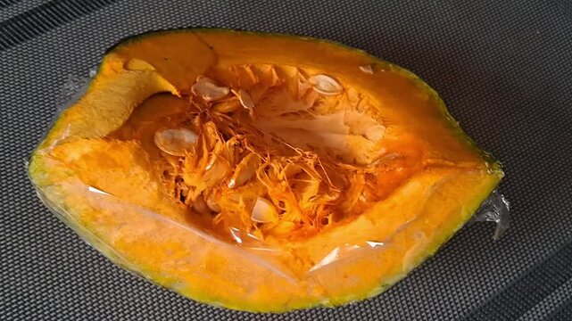 Freshly cut pumpkin slice wrapped in plastic film for preservation shown in a motion video clip
