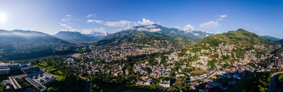 Aerial view of the city of Muzaffarabad nestled in a lush green valley with a winding river and towering mountains under a bright blue sky Muzaffarabad, Azad Kashmir, Pakistan.