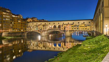 Fototapeta premium Cityscape with the Ponte Vecchio, a medieval stone arch bridge over the Arno, in Florence, Italy. Night view of the bridge. Long exposure. Family vacation in Italy.