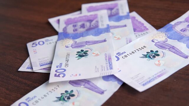 Close-up of Colombian fifty thousand pesos banknotes scattered on a dark wooden table, representing wealth and finance.