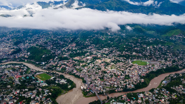 Aerial view of the city nestled in a valley at the confluence of rivers with lush green mountains and low clouds Muzaffarabad, Azad Kashmir, Pakistan.