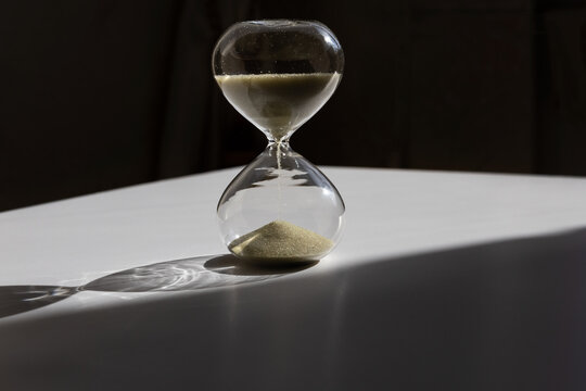Hourglass with golden sand illuminated by the sun on black background. Concept of aging and time. Selective focus and copy space