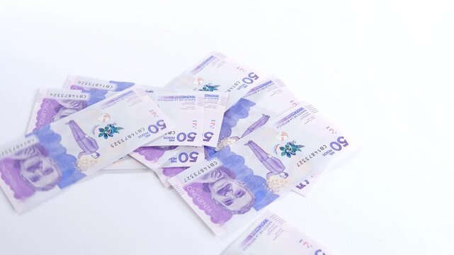 Scattered fifty thousand Colombian pesos banknotes spread across a clean white surface representing financial transactions