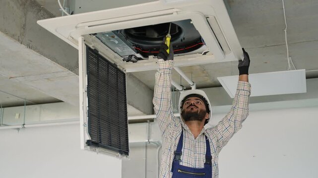 Technician repairing ceiling air conditioner with screwdriver