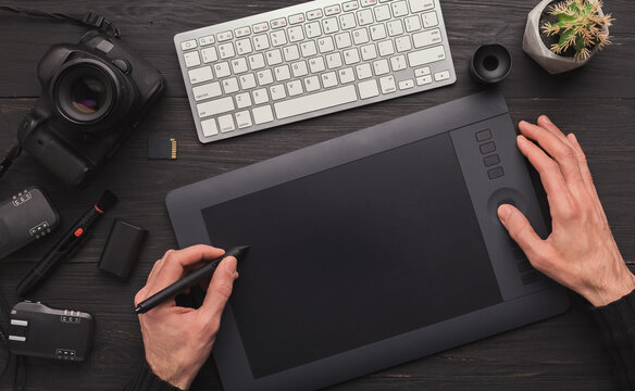 Top view on workplace of photographer. Creative designer hands working with computer keyboard and graphic tablet, photographic equipment on table