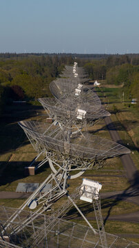Aerial view of the Westerbork Synthesis Radio Telescope with a long row of parabolic dishes stretching into the distance, with wind turbines on the horizon in Zwiggelte, Drenthe, Netherlands.