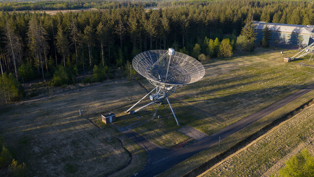 Aerial view of the Westerbork Synthesis Radio Telescope with its large parabolic antenna standing in a field surrounded by dense pine forest in Zwiggelte, Drenthe, Netherlands.