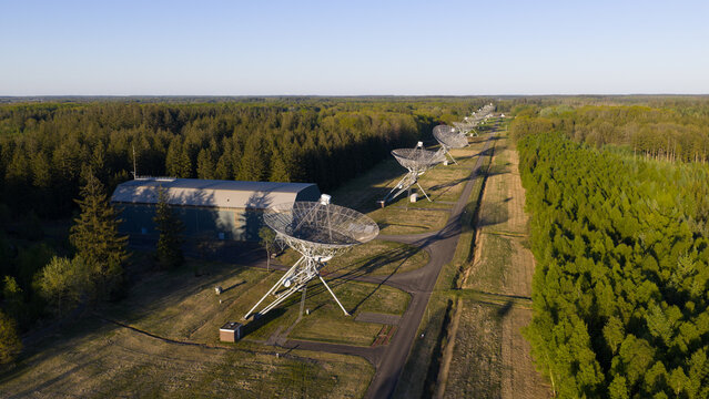 Aerial view of the Westerbork Synthesis Radio Telescope dishes aligned in a row amidst a dense green forest under a clear sky in Zwiggelte, Drenthe, Netherlands.