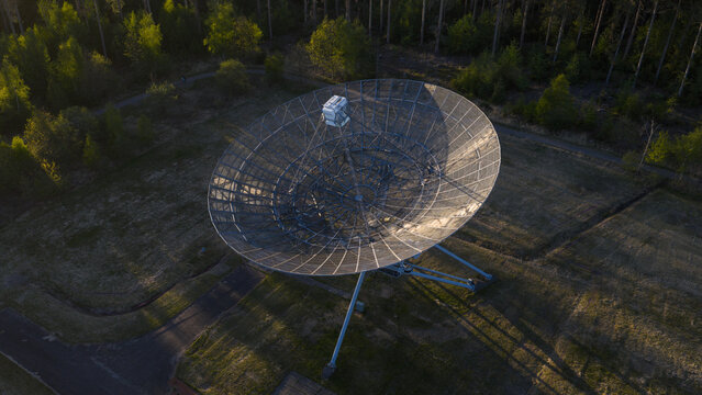 Aerial view of the Westerbork Synthesis Radio Telescope dish surrounded by lush forest during golden hour in Zwiggelte, Drenthe, Netherlands.