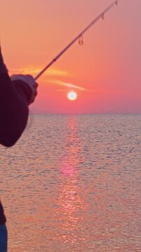 Vertical video. Fishing Rod Pointing Toward Setting Sun Over Sea Horizon Close Perspective Warm Light Reflection Outdoor Angling Scene