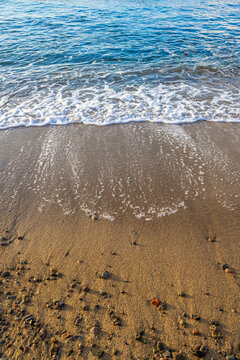 Calm sea wave gently reaching sandy beach with subtle foam and pebbles.