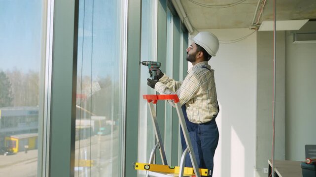 Male construction worker installing windows with drill
