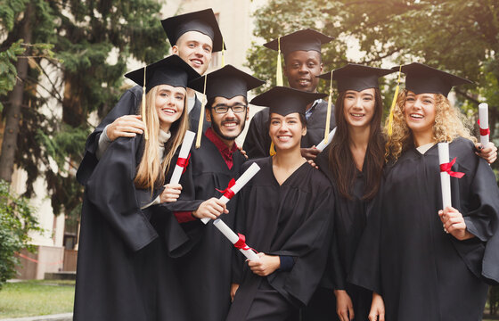 A group of multiethnic students hugging on their graduation. Education, qualification and gown concept.