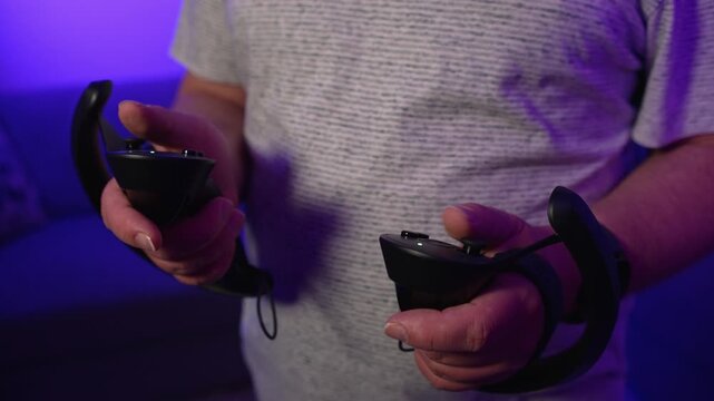 Close up of hands holding VR controllers controlling virtual reality demonstrating interaction with digital environment and precise control in gameplay in neon lighting
