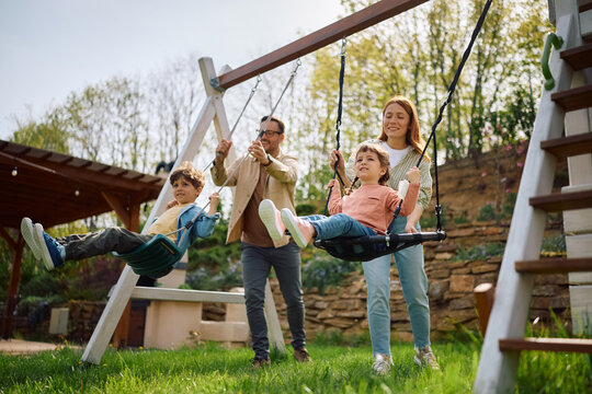 Happy parents pushing their kids on swing at park.