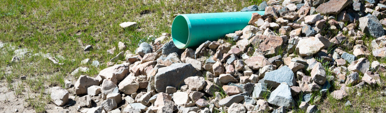 New industrial plastic pipe sticking out of a dirt hillside, onto rocks to prevent erosion, for stormwater to spill into a water retention pond
