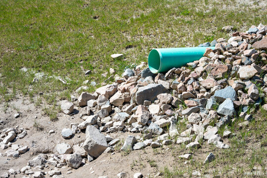 New industrial plastic pipe sticking out of a dirt hillside, onto rocks to prevent erosion, for stormwater to spill into a water retention pond
