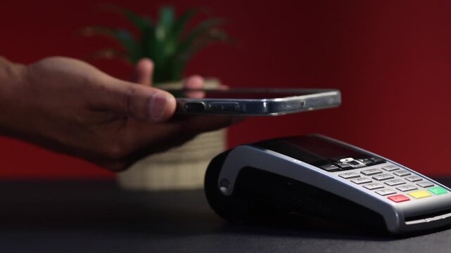 Customer's hand holding a smartphone making a contactless payment on a pos terminal, demonstrating near field communication technology for convenient and fast checkout