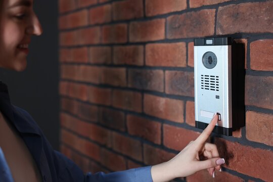 Woman pressing button on intercom panel near brick wall, closeup