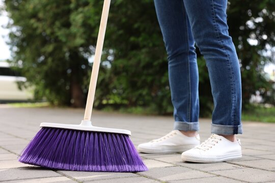Woman with broom sweeping pavement outdoors, closeup