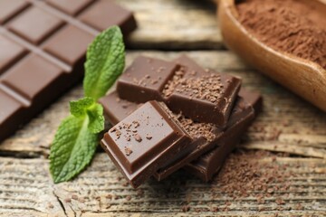 Pieces of yummy chocolate, mint leaves and cocoa powder on wooden table, closeup © New Africa
