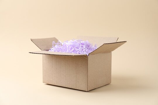 Cardboard box with shredded paper filler on beige background