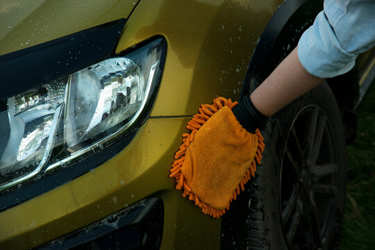 Man holds the microfiber gloves in hand and washes the car headlight with detergent. Car detailing. Selective focus