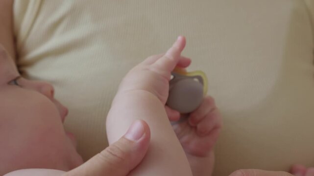 Gentle maternal bond close up. Calm morning moment with mother and infant peacefully interacting on bed. baby studies pacifier with tiny hands, concentrated gaze toward object. calm atmosphere