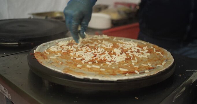 Chef sprinkles cheese and toppings on street food pancake Indian Dosa Roti