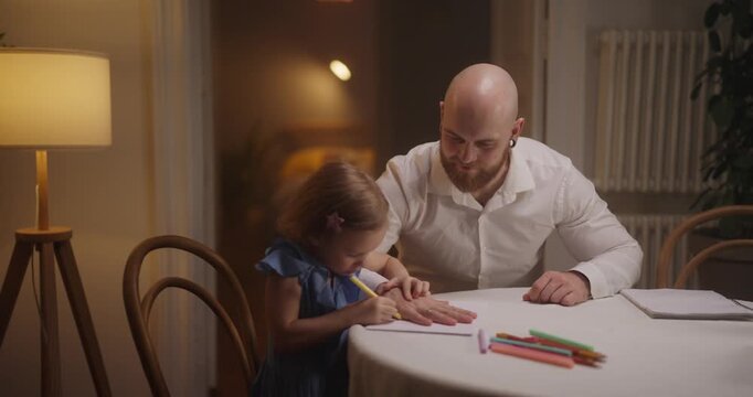 A joyful father helps his daughter express herself through drawing, sharing smiles and colorful crayons in a warm room