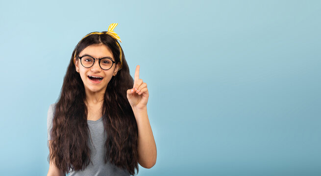 Great idea concept. Excited Indian teen girl pointing finger up, finding creative solution to problem, having aha moment on blue studio background, banner with free space. Wow, eureka