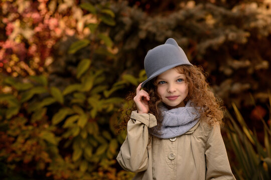 Little cute smiling girl in funny cat hat with long curly hair. Autumn seasonal portrait of young girl outdoor in the garden. Kid fall portrait. Child in the autumn garden. Selective focus, close up