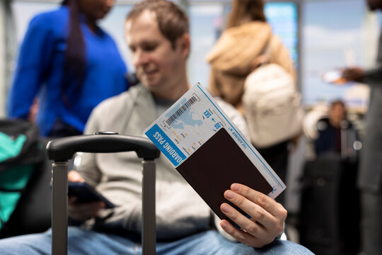 Close up of man holding passport and boarding pass inside airport lounge. Passenger preparing travel documents for customs before international departure during long flight layover