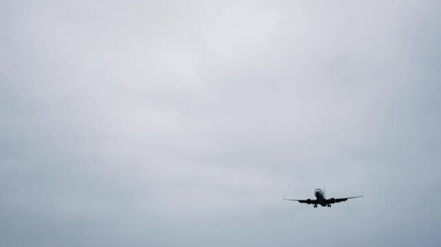 Dark silhouette of large passenger airplane, airliner is flying in the dramatic gray sky - slow motion. Transportation, mystery, gloomy and flight concept