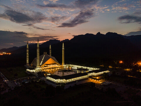 Aerial view of Faisal Masjid illuminated at dusk with the Margalla Hills in the background under a cloudy sunset sky Islamabad, Islamabad Capital Ter, Pakistan.