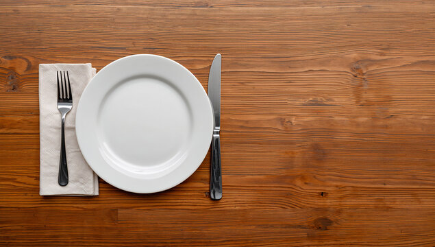 木目の卓上で白い皿とカトラリーが食事の準備を整えている